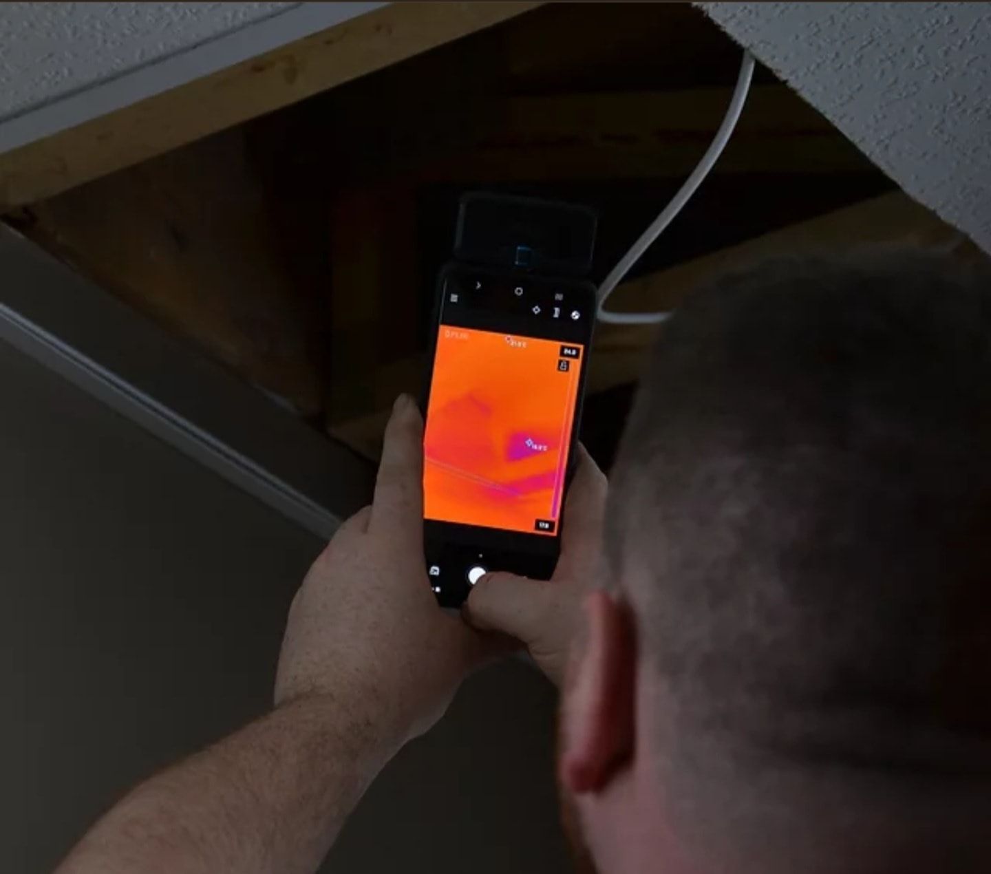 Une personne utilise un smartphone avec imagerie thermique pour inspecter une cavité de plafond, montrant des schémas de chaleur.
