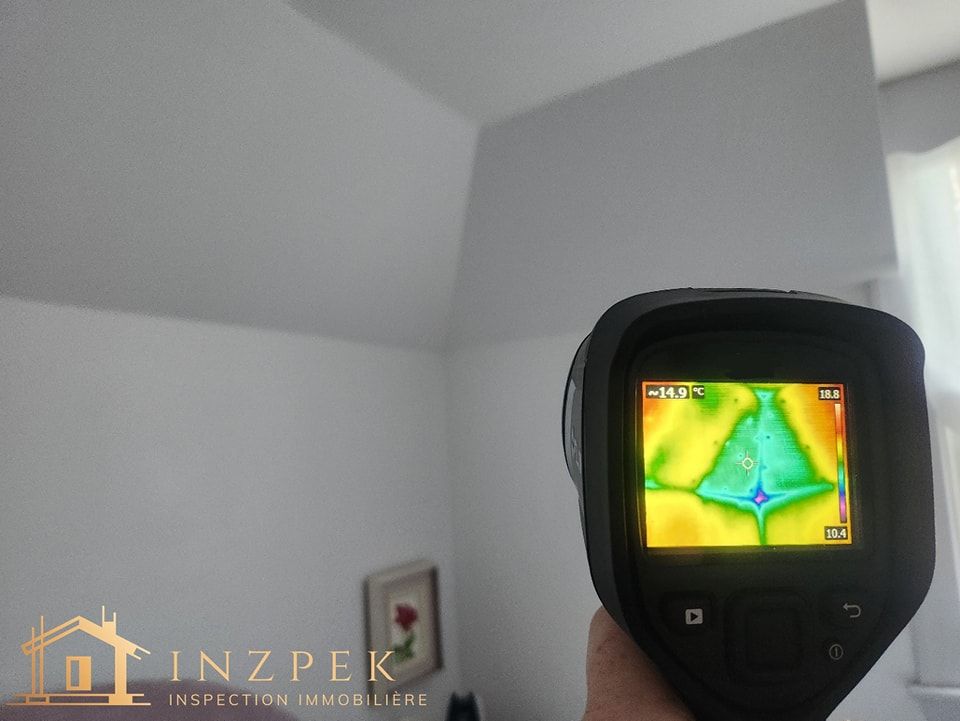 Une caméra thermique montre un point froid au plafond ; une personne tient l'appareil.