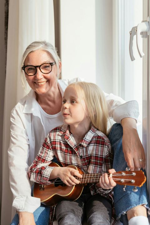 An elderly woman is sitting next to a little girl playing a ukulele.