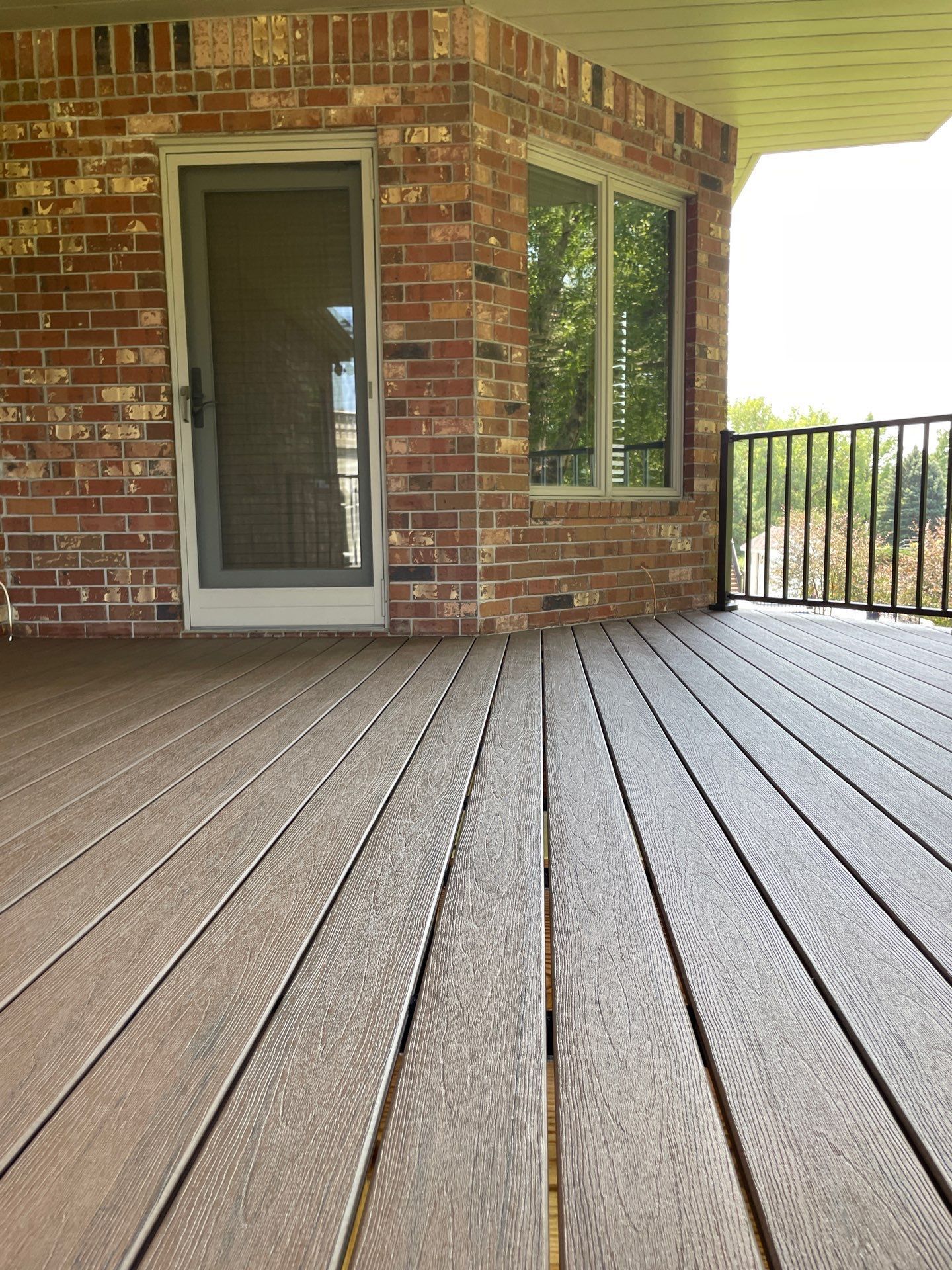 A wooden deck with a brick building in the background and a sliding glass door.