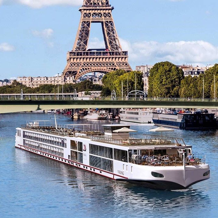 The eiffel tower is visible behind a river cruise in the water in Paris