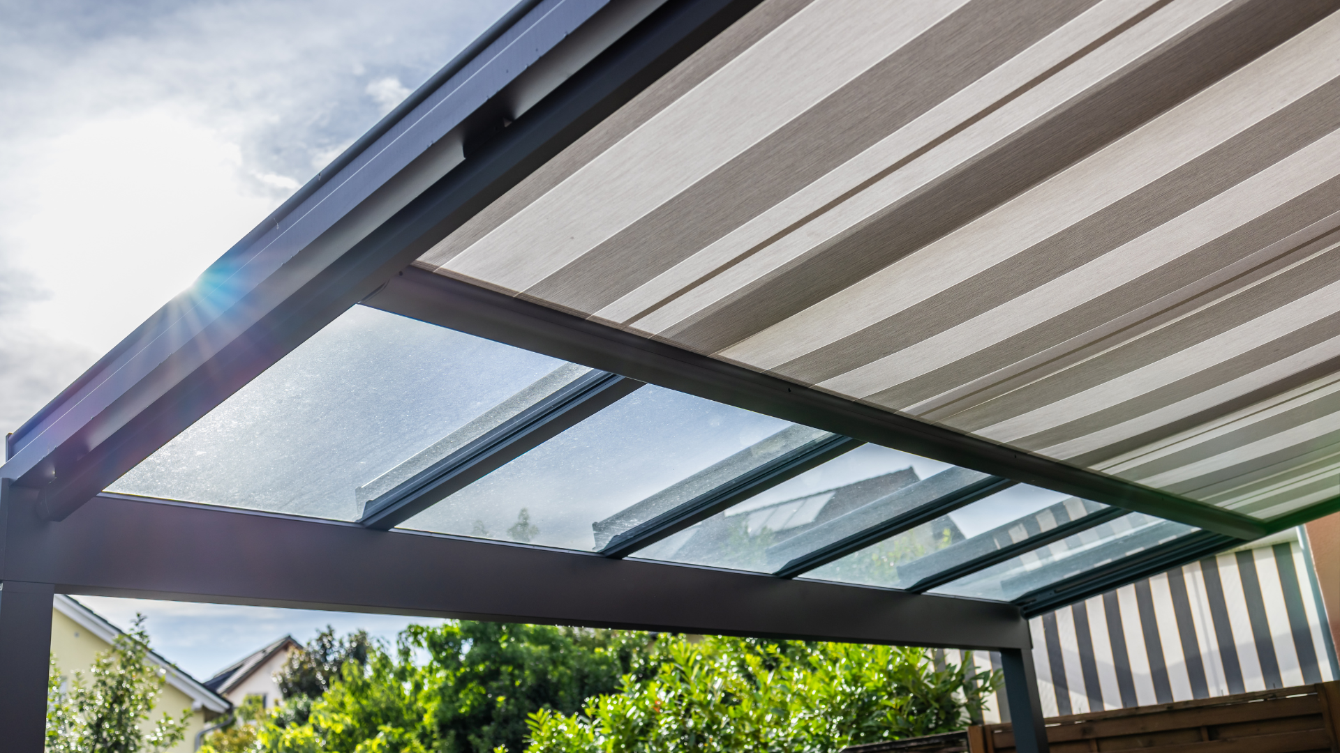 Pergola roof with striped shade and glass panels, with a glimpse of sky.