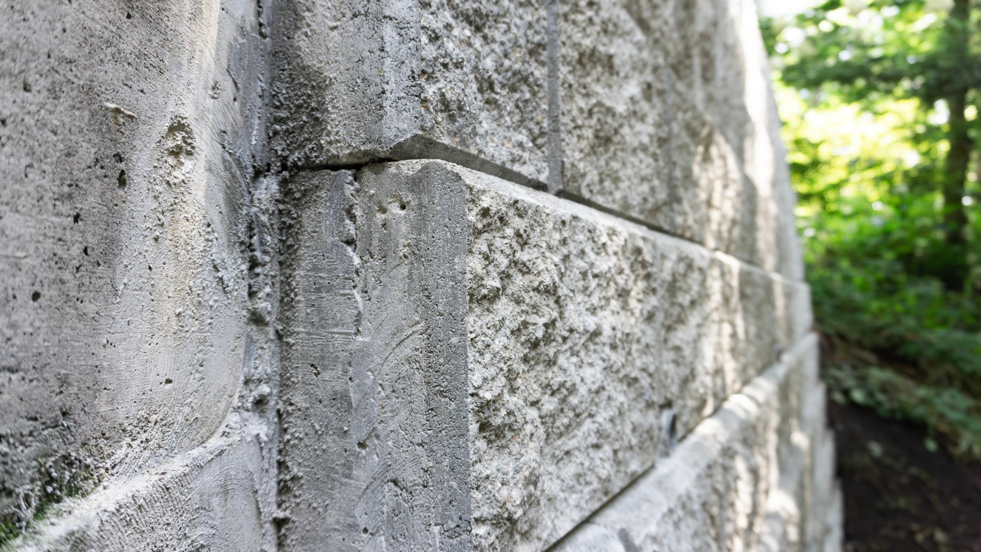 Close-up of a gray concrete block retaining wall. Angled view shows textured surface and seams.