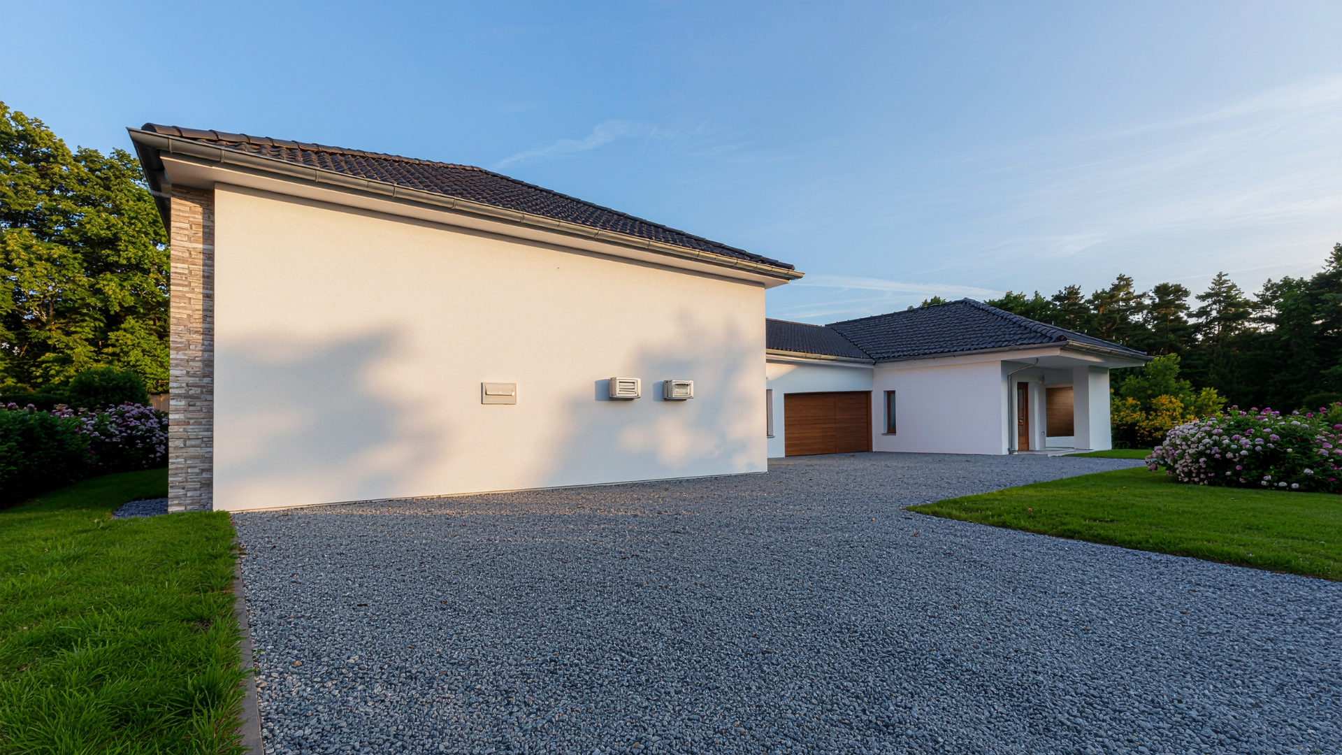 Modern house with white walls, gravel driveway, and green lawn.