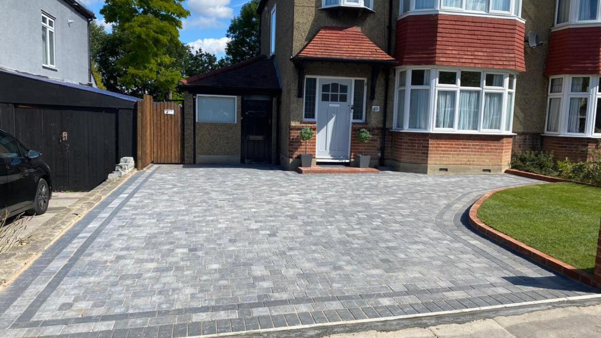 Driveway with gray paving stones leading to a house with a red brick facade and front door.
