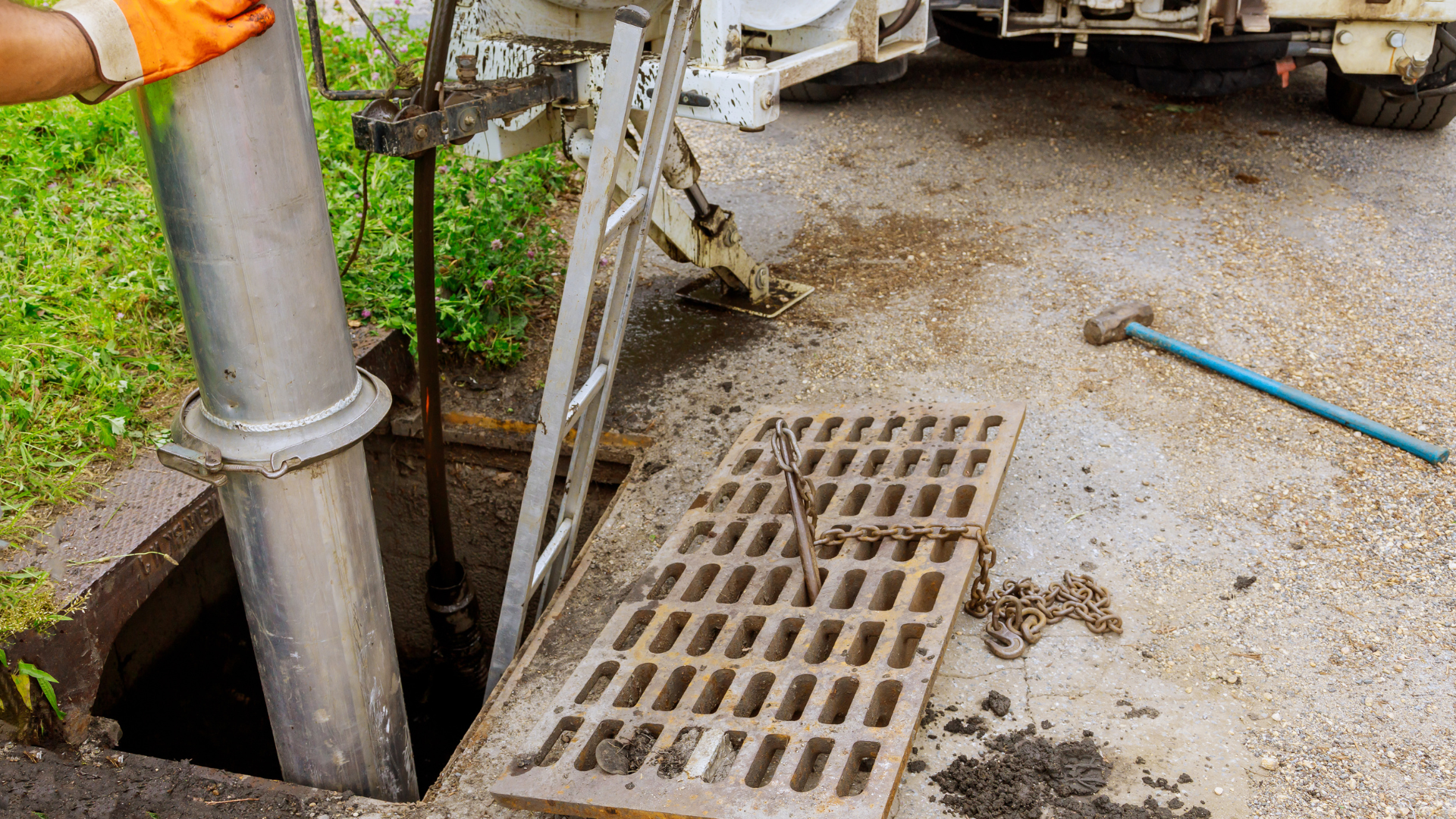 A worker in orange gloves lowering a large pipe into an open manhole on a street.