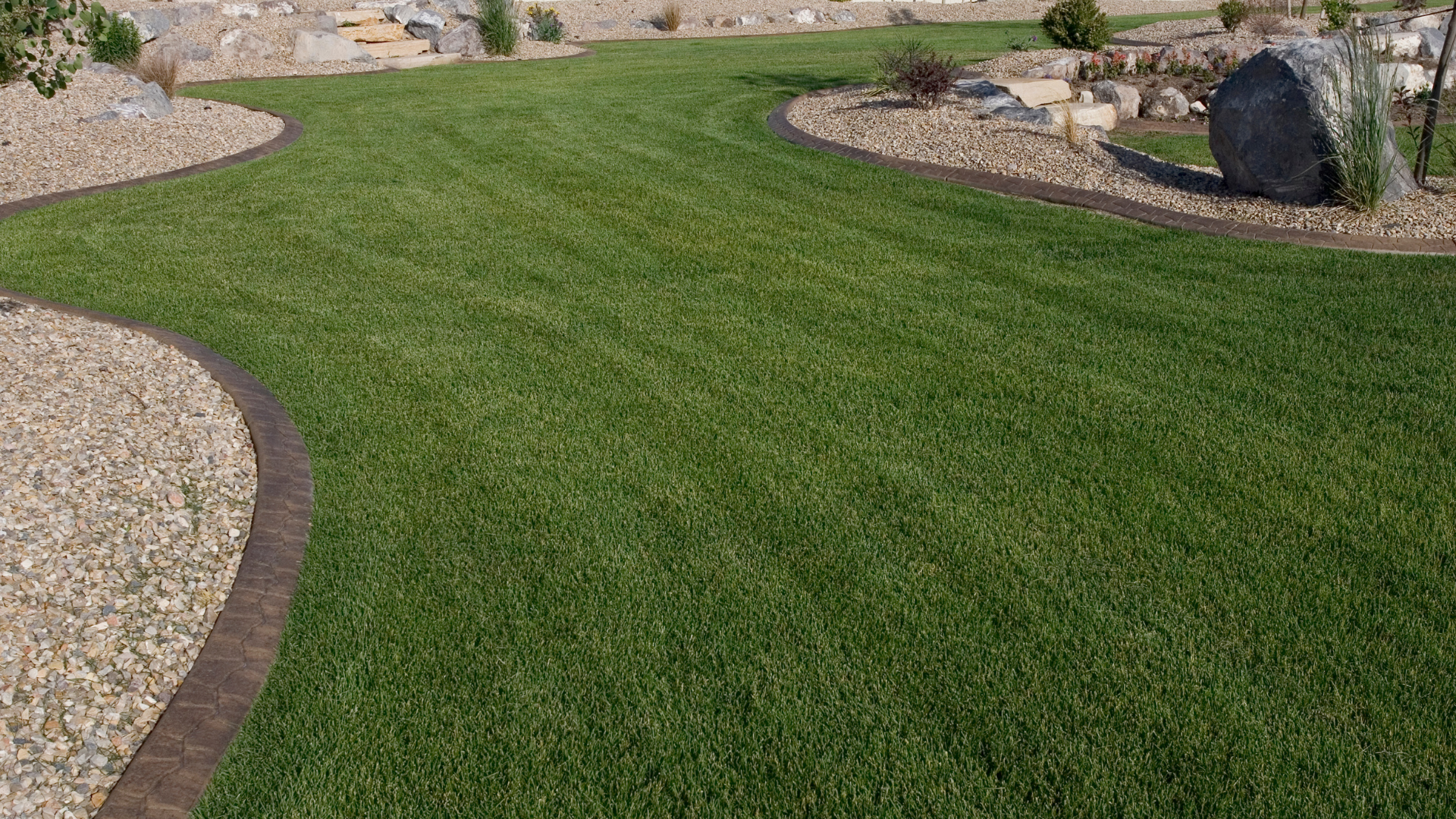 Lush green lawn with curved brown borders alongside tan gravel beds.