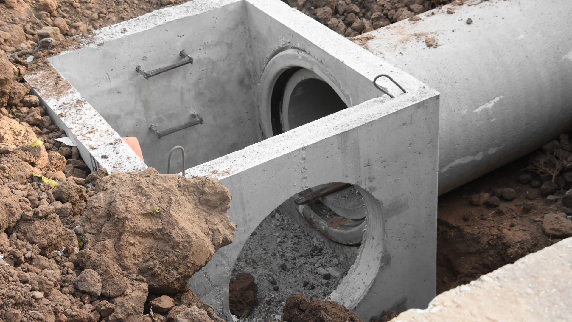 Concrete drainage system construction in a dirt pit. A pipe connects to a square concrete structure.