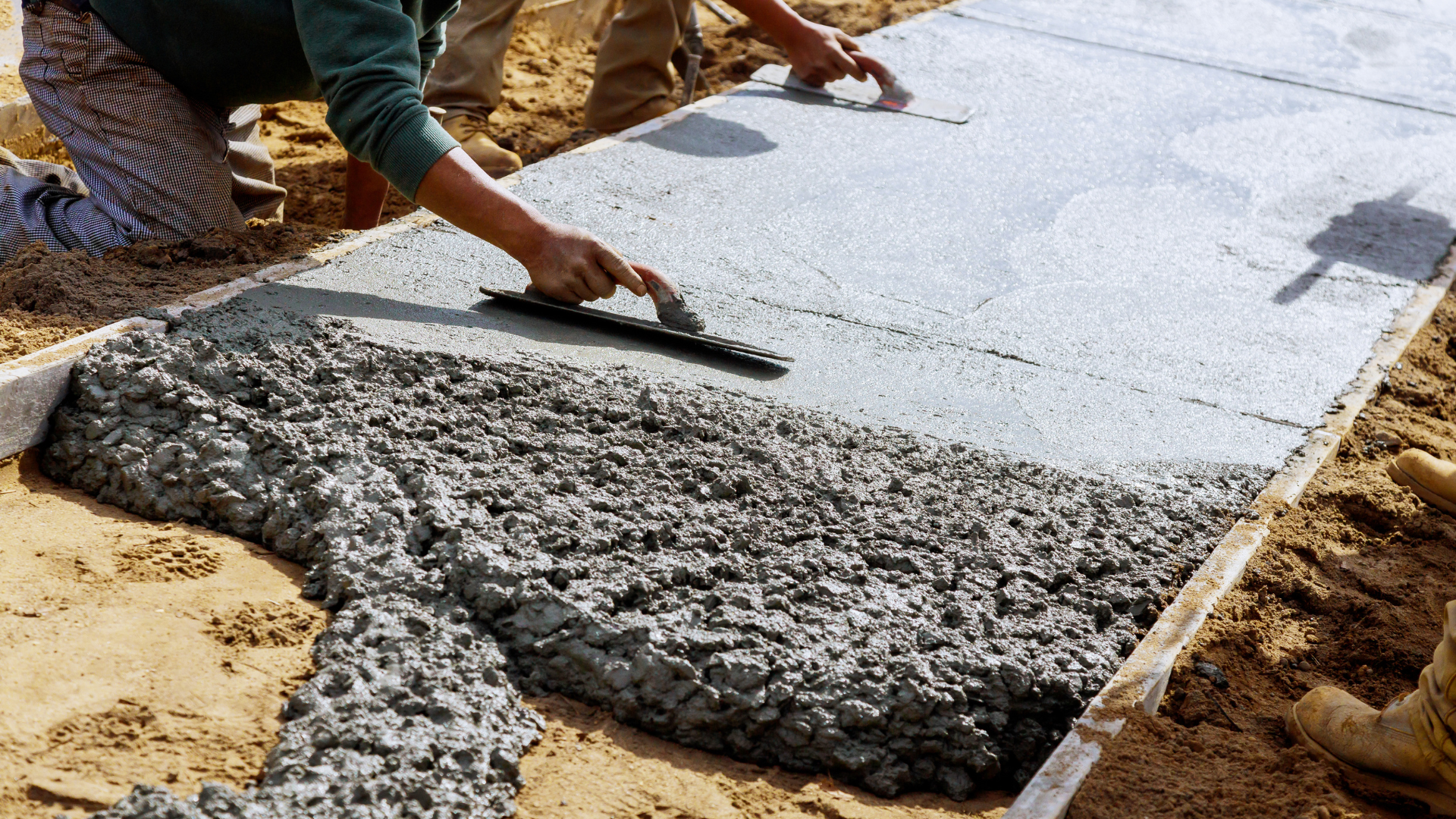Workers smoothing wet concrete in a form, preparing a sidewalk.