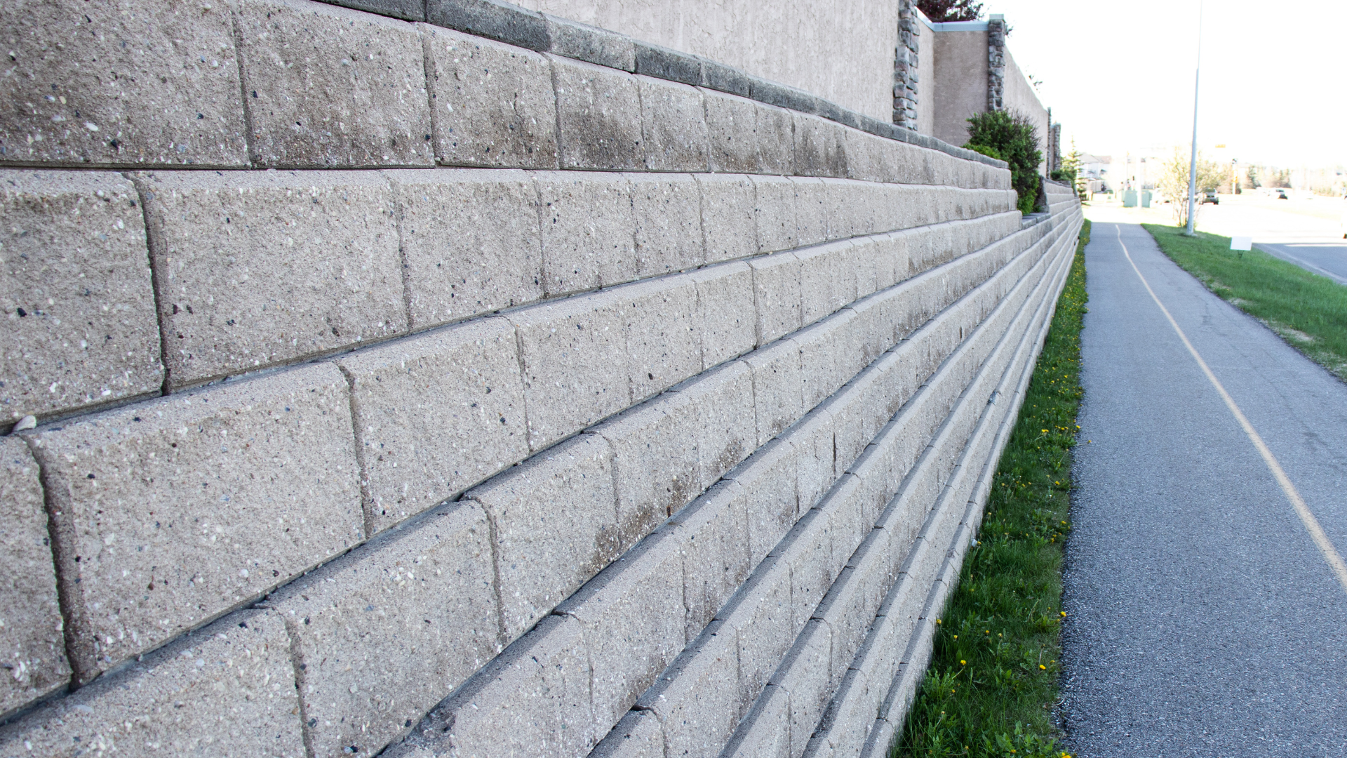 Gray concrete retaining wall alongside a paved path and grass.