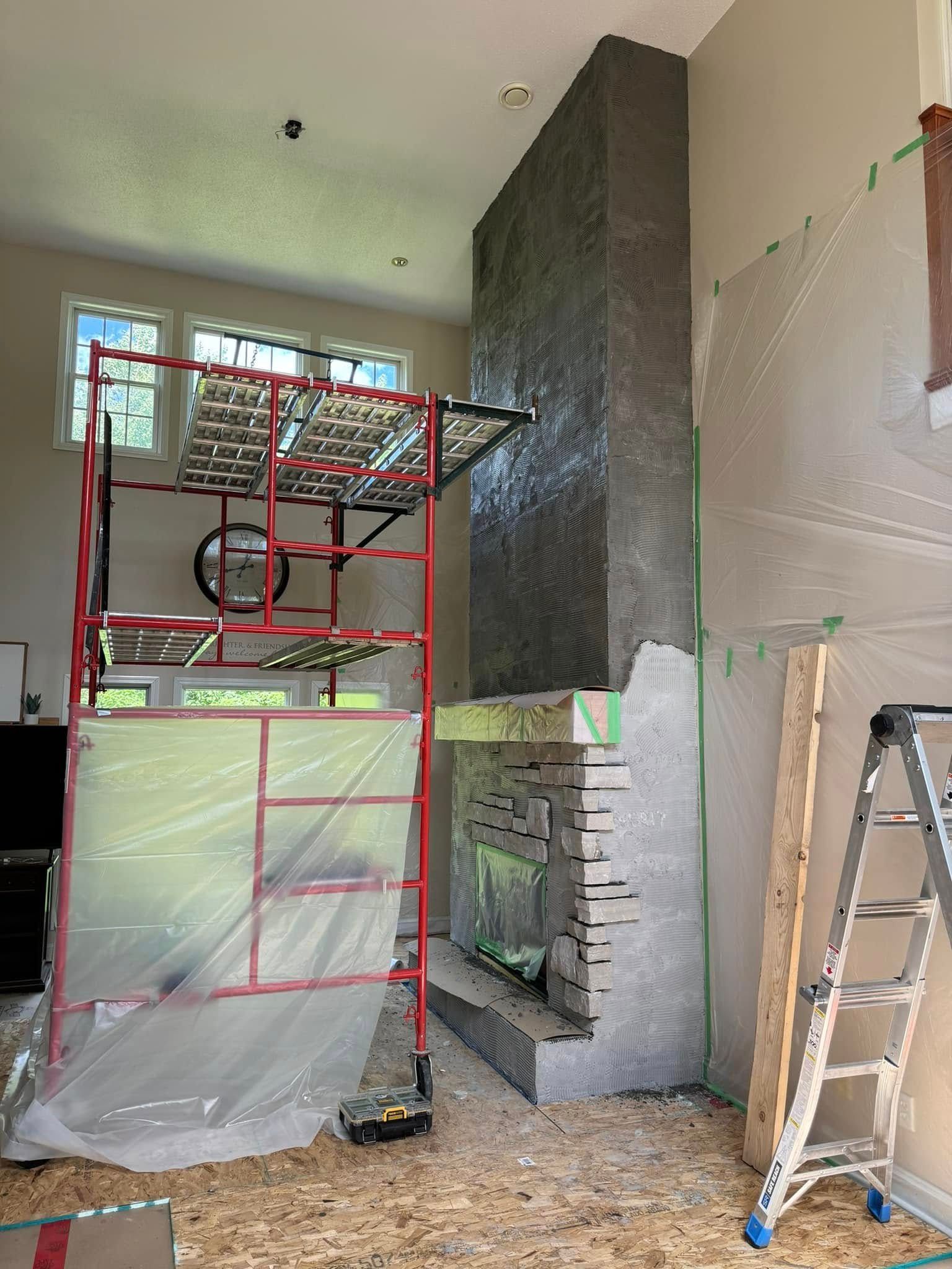 Fireplace under construction, covered in gray concrete. Red scaffolding with plastic sheeting, ladder and masked walls.