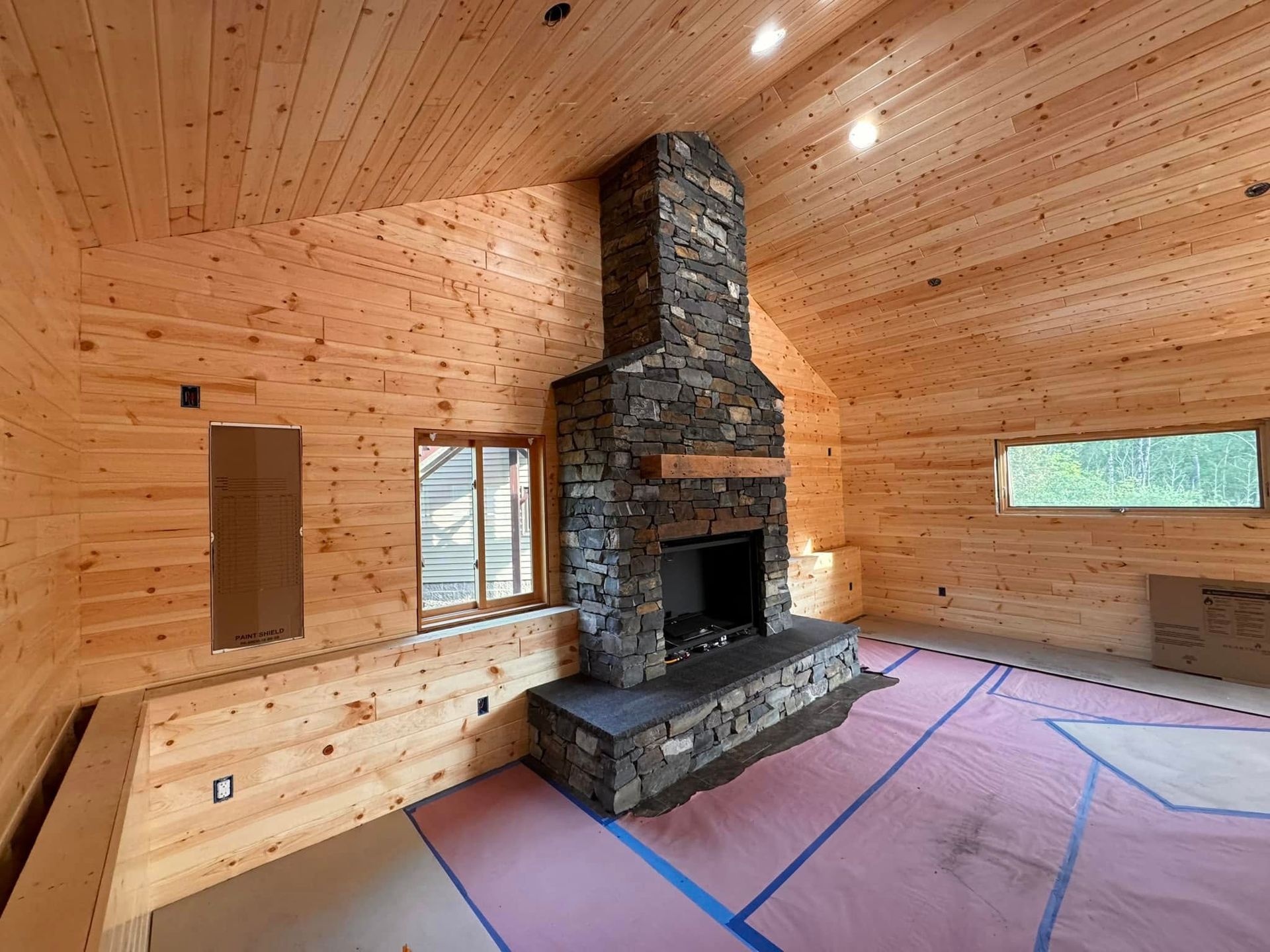 Interior of a cabin with a stone fireplace, wood walls, and a protective floor covering.