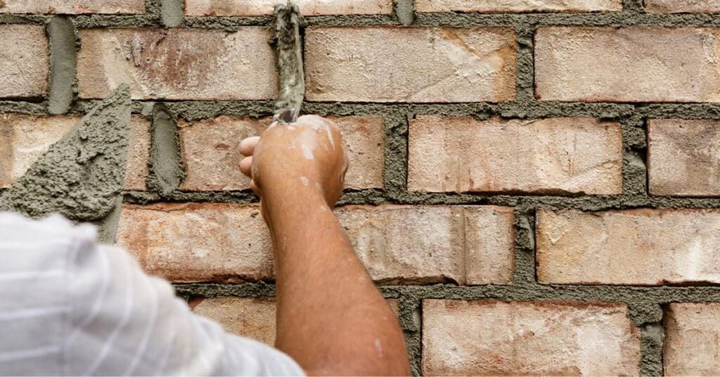 A person's hand smoothing mortar between bricks on a wall.