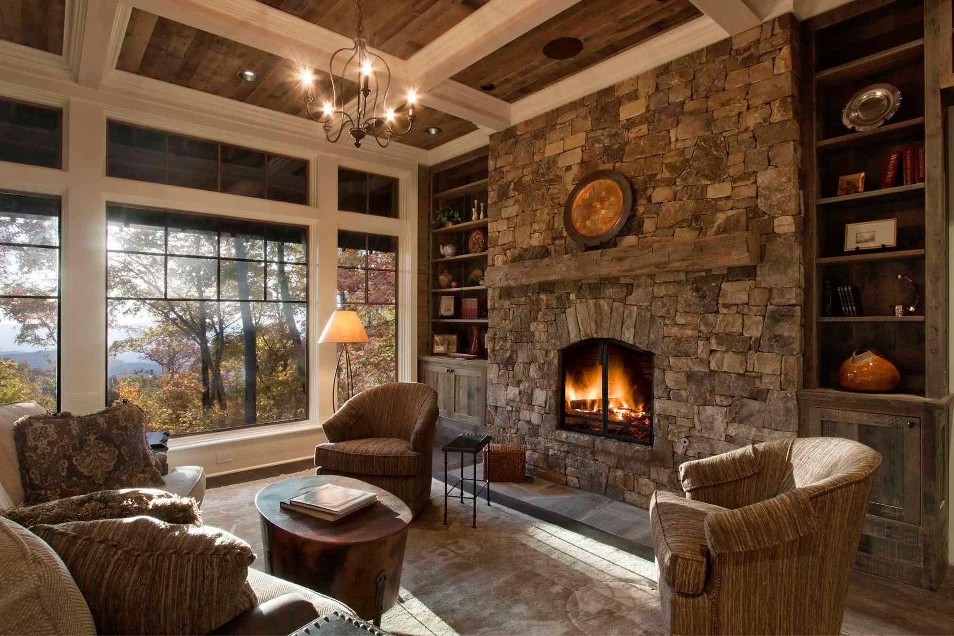 Cozy living room with stone fireplace, built-in shelves, large windows with a view, and comfortable seating.
