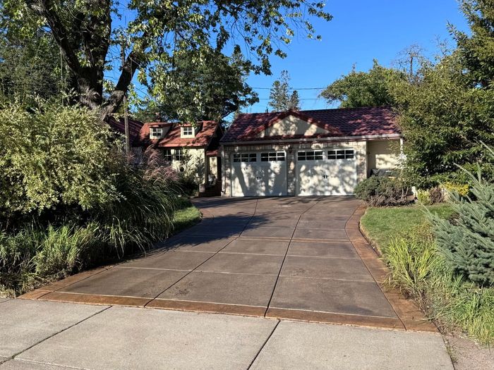 Driveway leading to a yellow house with a garage, surrounded by trees under a blue sky.