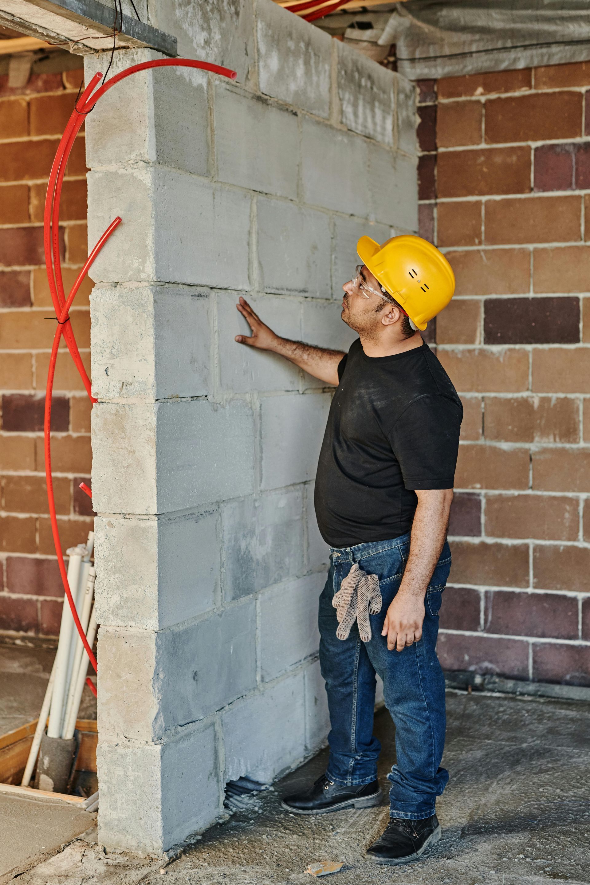 A worker in a hard hat inspects a newly constructed cinder block wall inside a building under renovation.