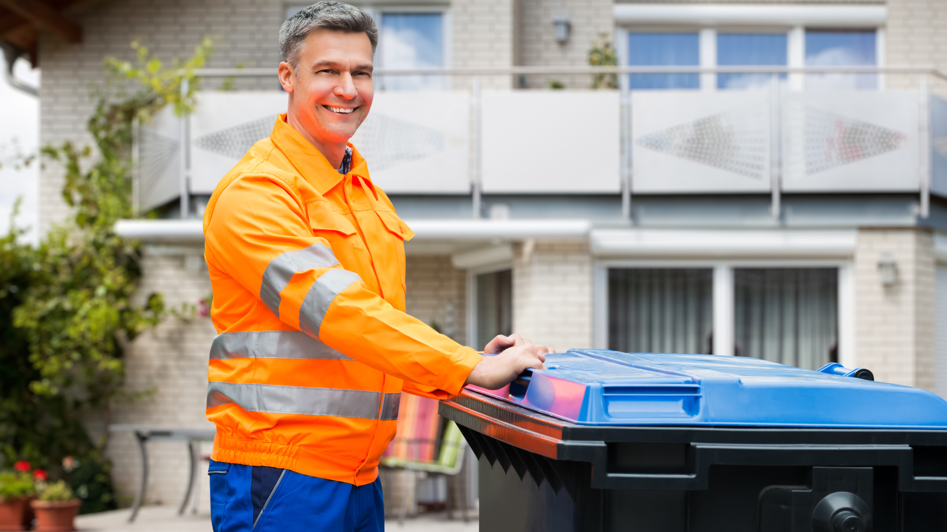 A man is standing next to a trash can in front of a house.