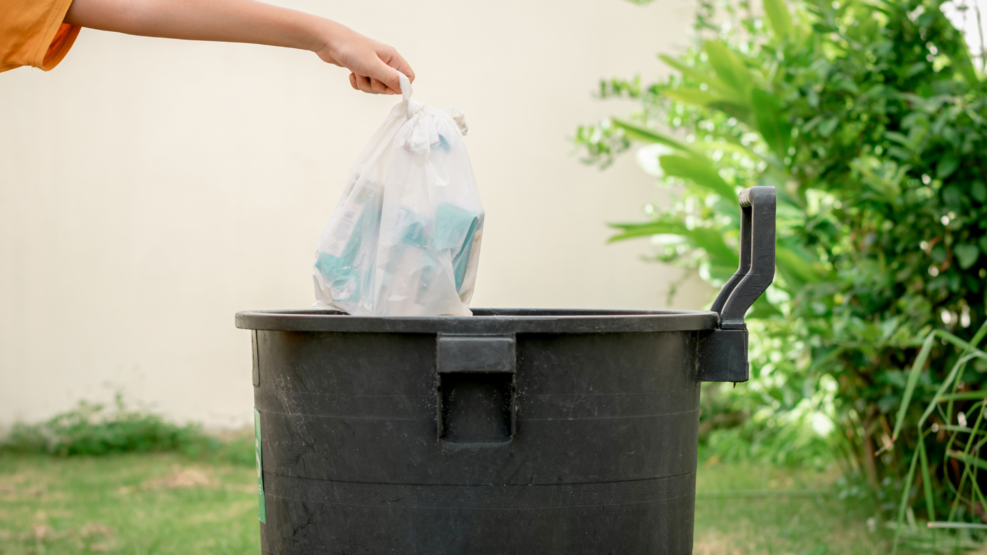 A person is throwing a plastic bag into a trash can.