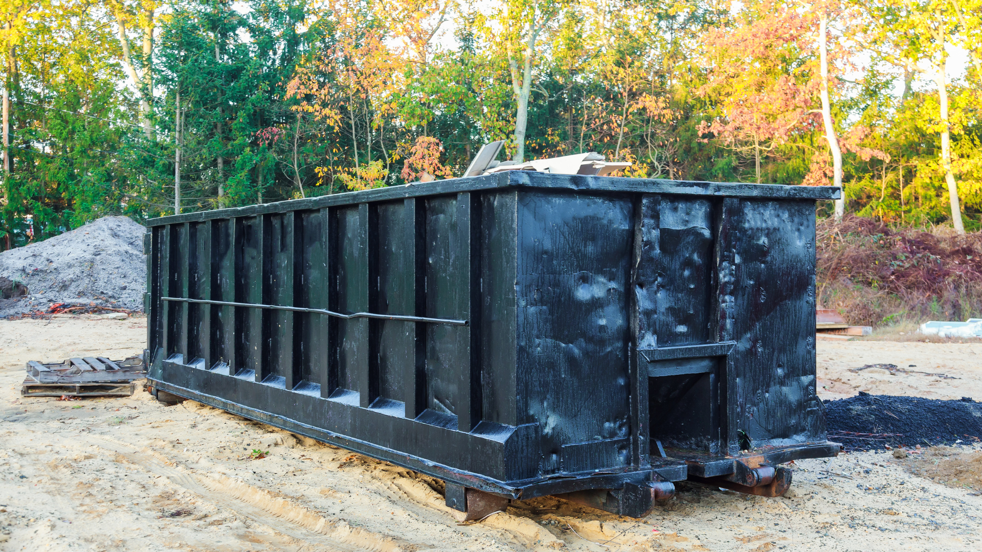 A large black dumpster is sitting in the middle of a dirt field.