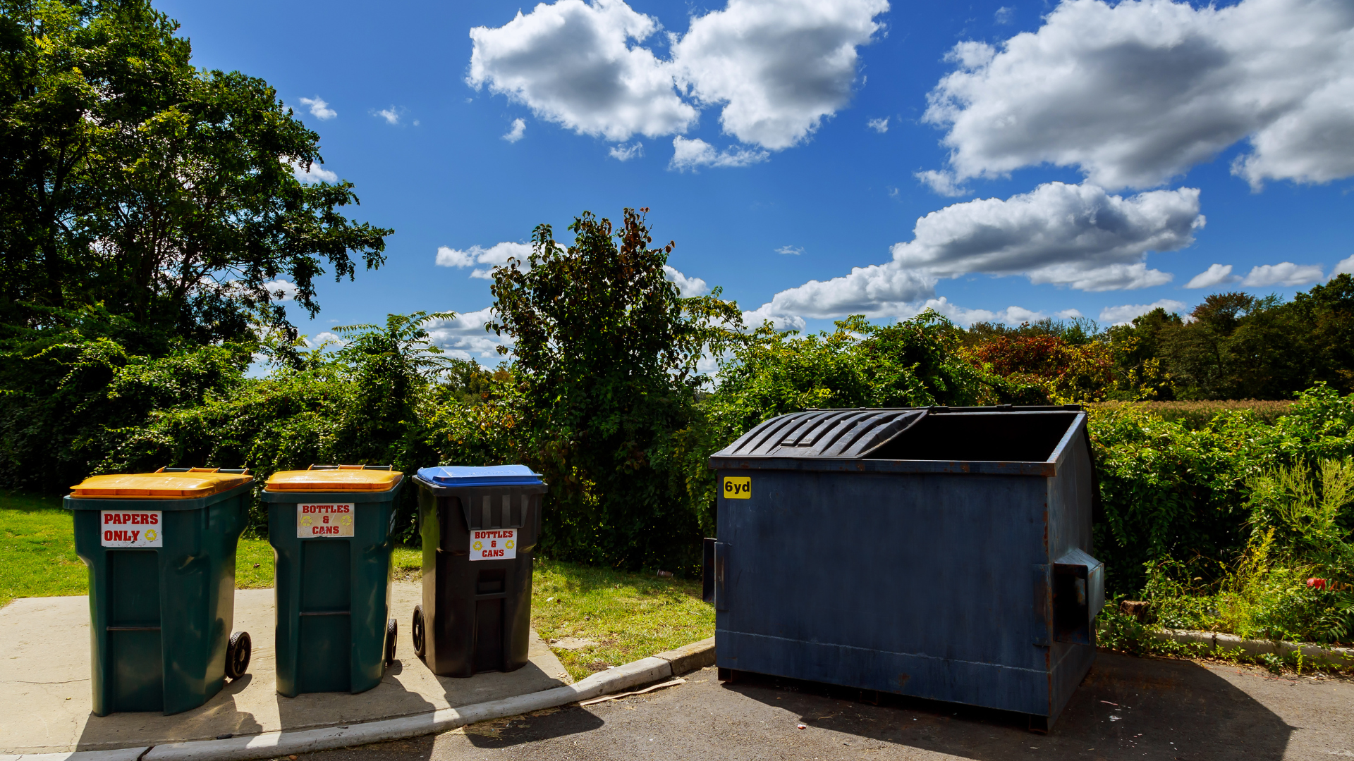 Three garbage cans are lined up next to a dumpster.