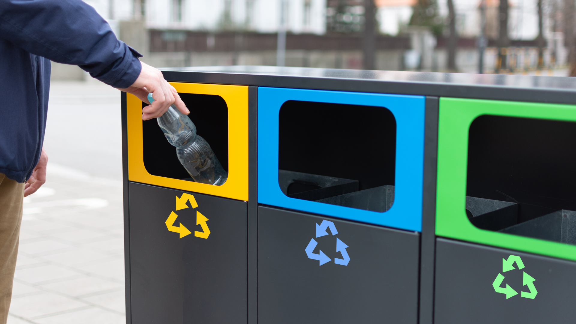 A man is throwing a plastic bottle into a recycling bin.