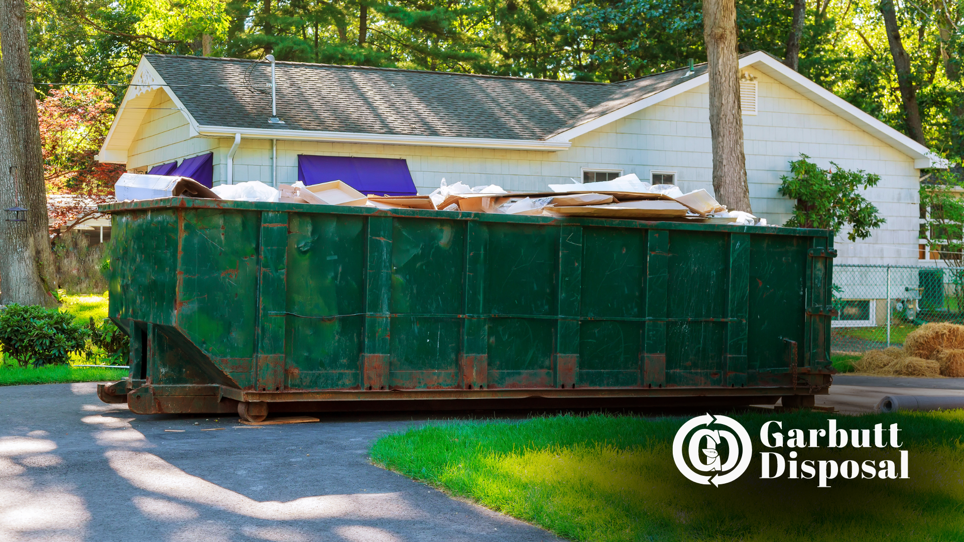 A large green dumpster is parked in front of a house.