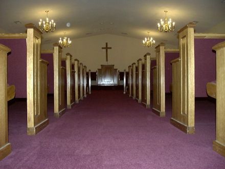 Empty chapel interior with purple carpet, wooden pews, and a cross.