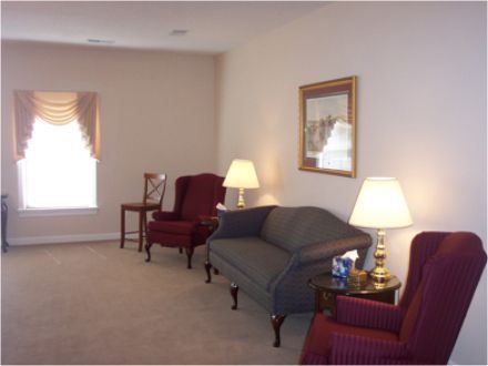 Living room with chairs, sofa, lamps, and a window with a valance. Beige walls and carpet.