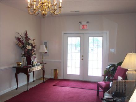 Interior lobby with red carpet, double doors, and a small table with floral arrangement.