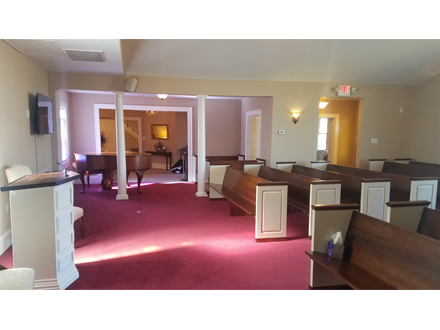 Interior of a funeral home with rows of wooden pews, a podium, and a piano on a red carpet.