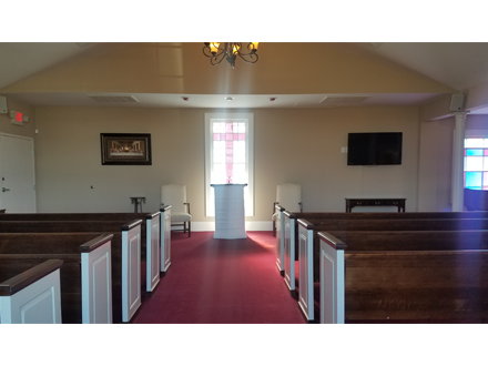 Interior of a church with rows of pews, a red carpet, and a central podium in front of a window.