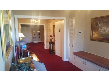 Hallway with red carpet, neutral walls, bench, and artwork. Open doorways lead to additional rooms.