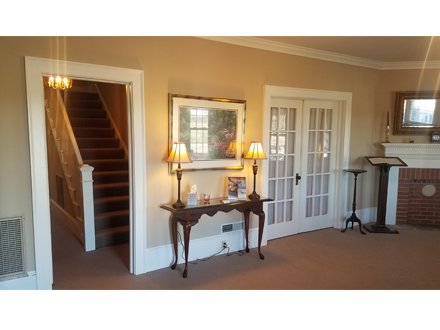 A room with a staircase, table with lamps, framed mirror, double doors, and a fireplace.