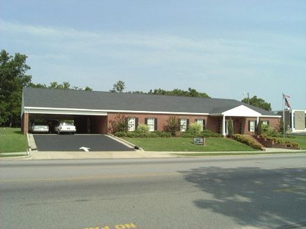 Brick building with carport; white cars parked. American flag on right.