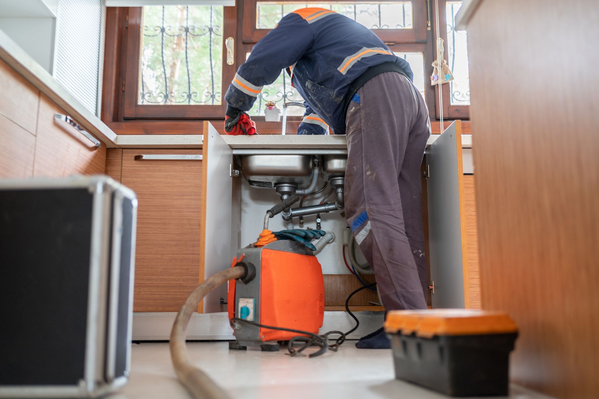 A plumber is fixing a sink in a kitchen with a vacuum cleaner.