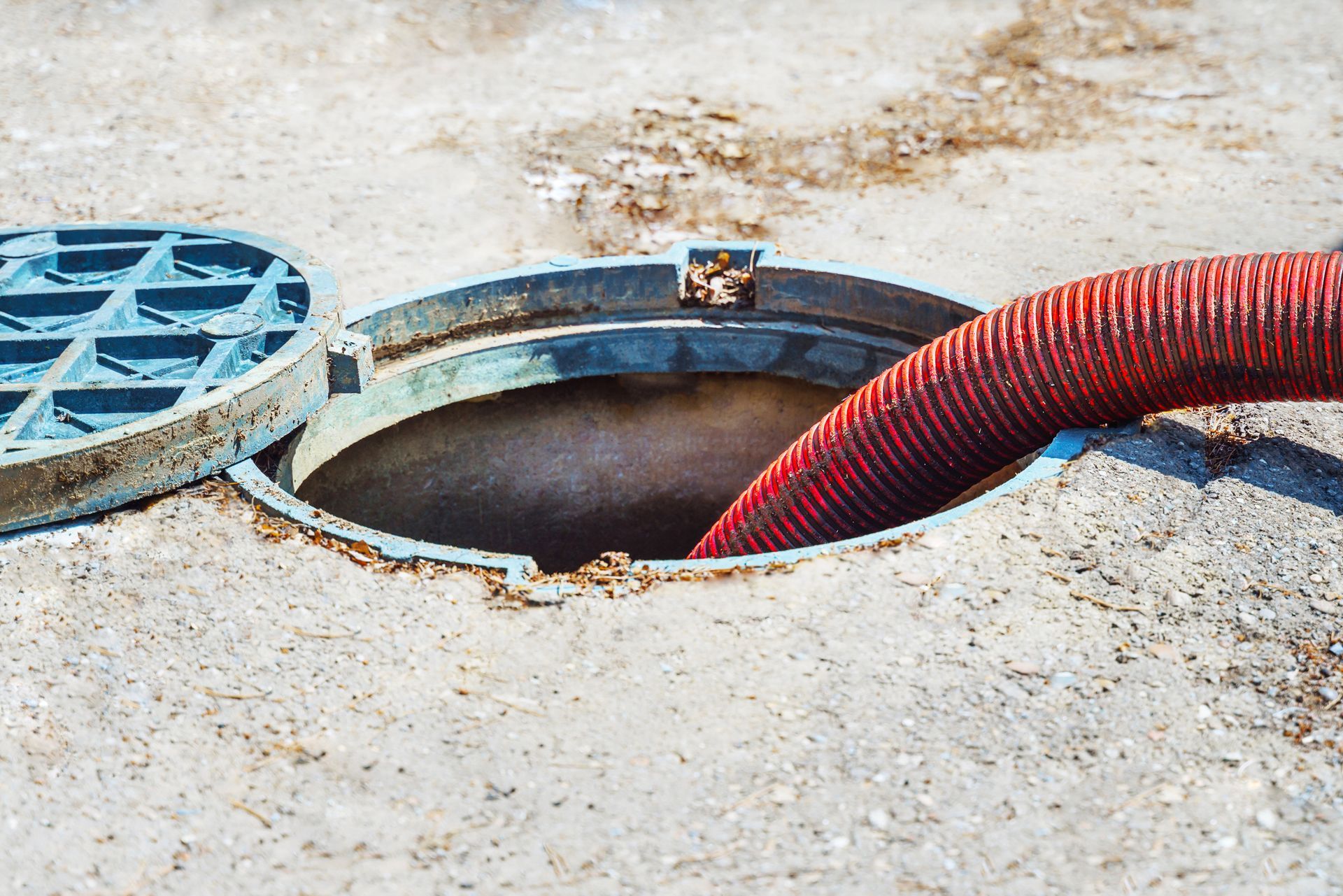 Close-up image of a red hose inserted into an open manhole on a concrete surface.