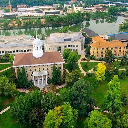 An aerial view of a large building surrounded by trees and a river.