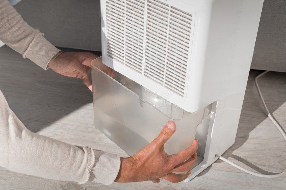 A man changing the water container in an air dryer or dehumidifier with a humidity indicator. Addressing humid air at home.