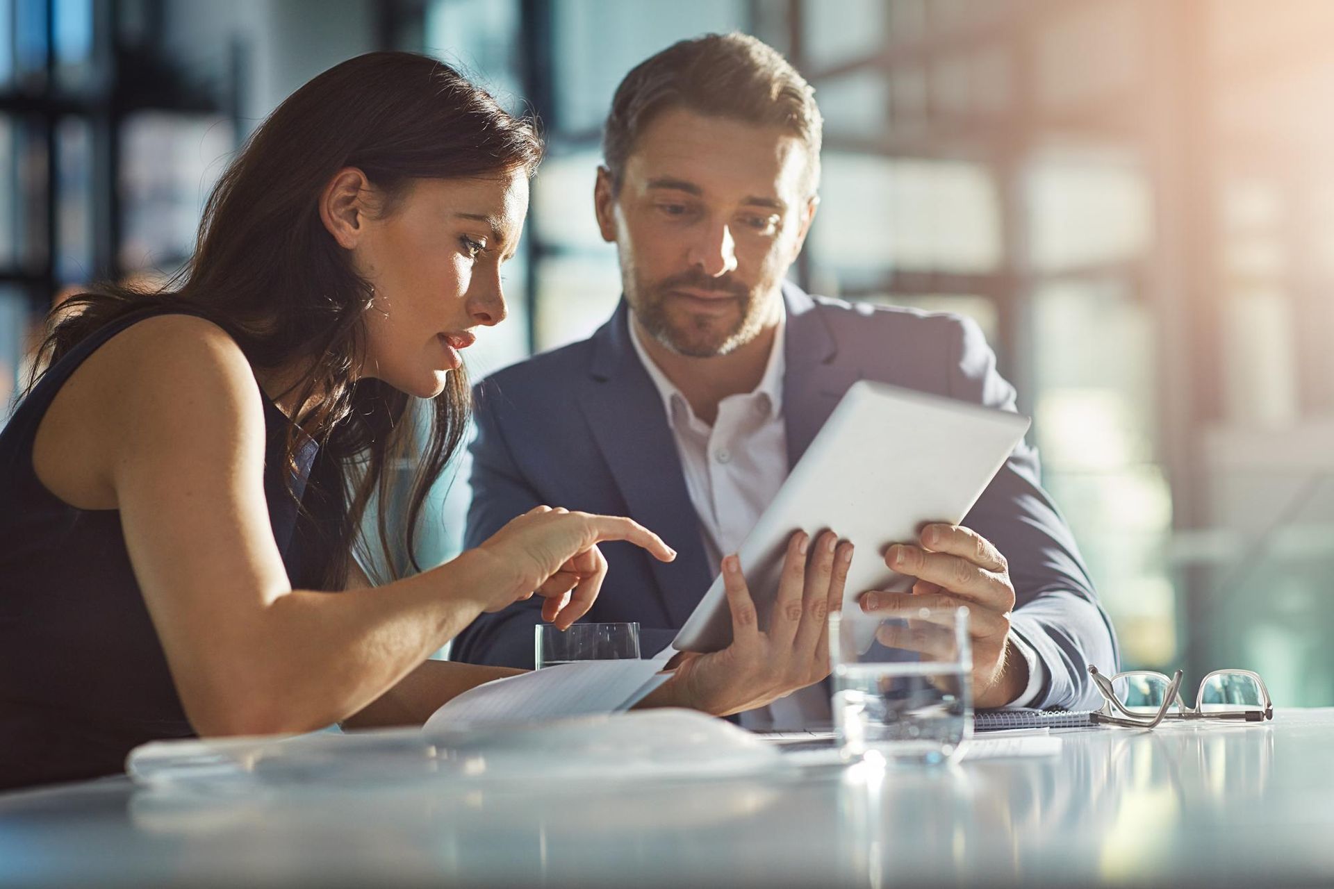 A man and a woman are sitting at a table looking at a tablet.