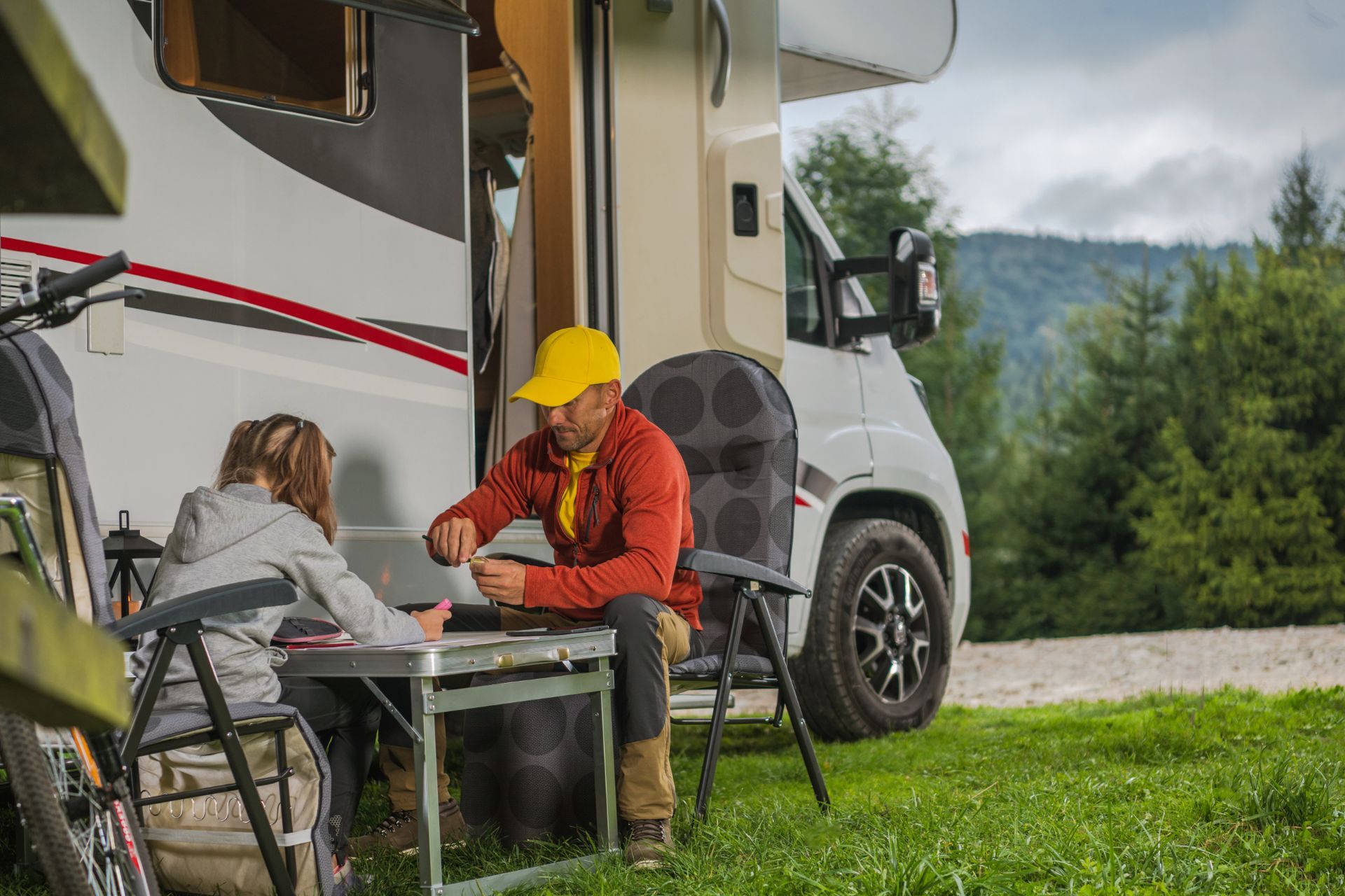 A man and a woman are sitting outside of a rv.