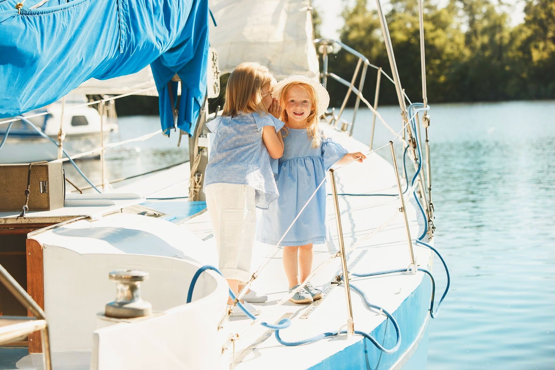 Two little girls are standing on a sailboat in the water. 
