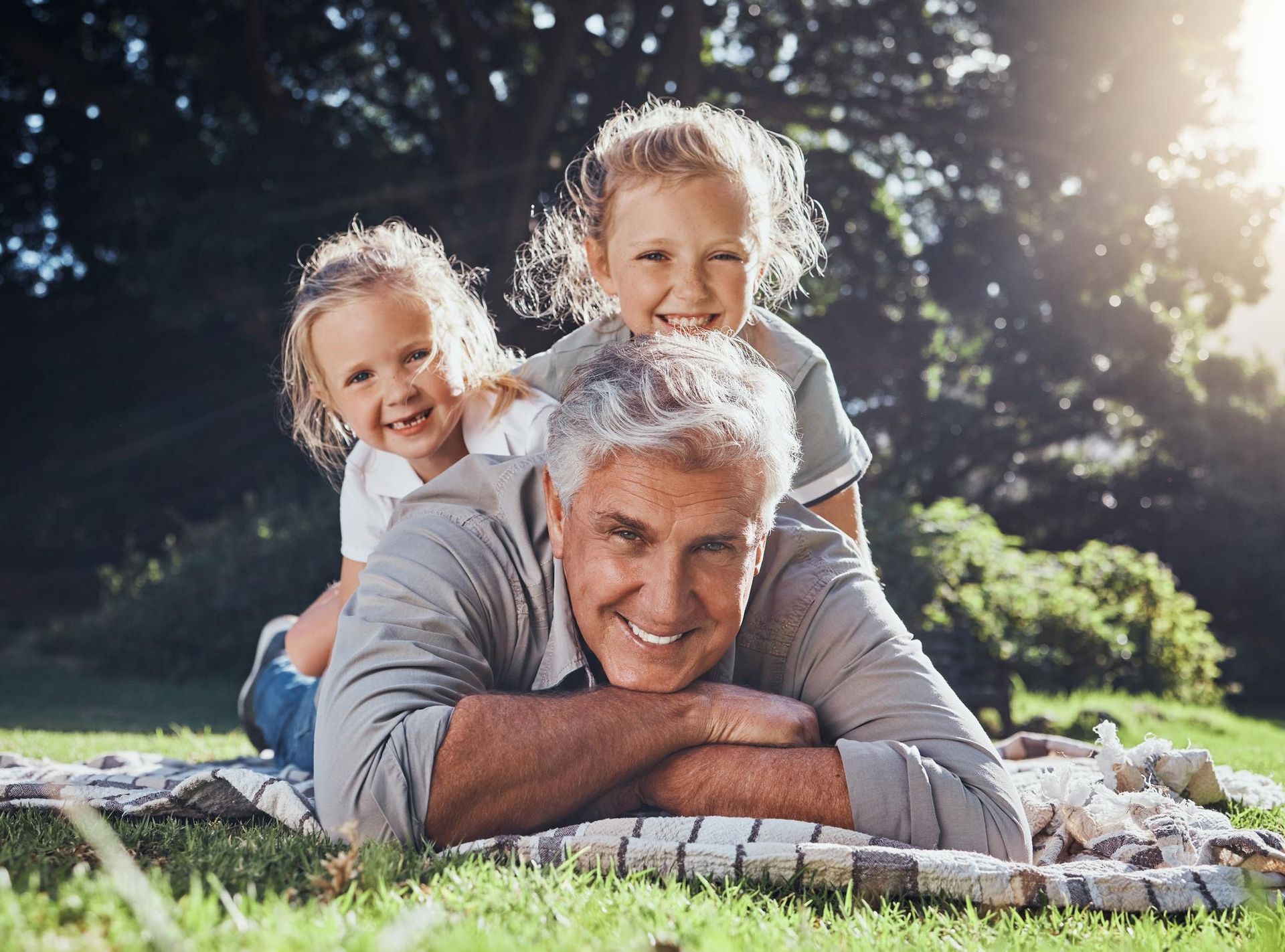 A man is laying on a blanket with two little girls on his back. 
