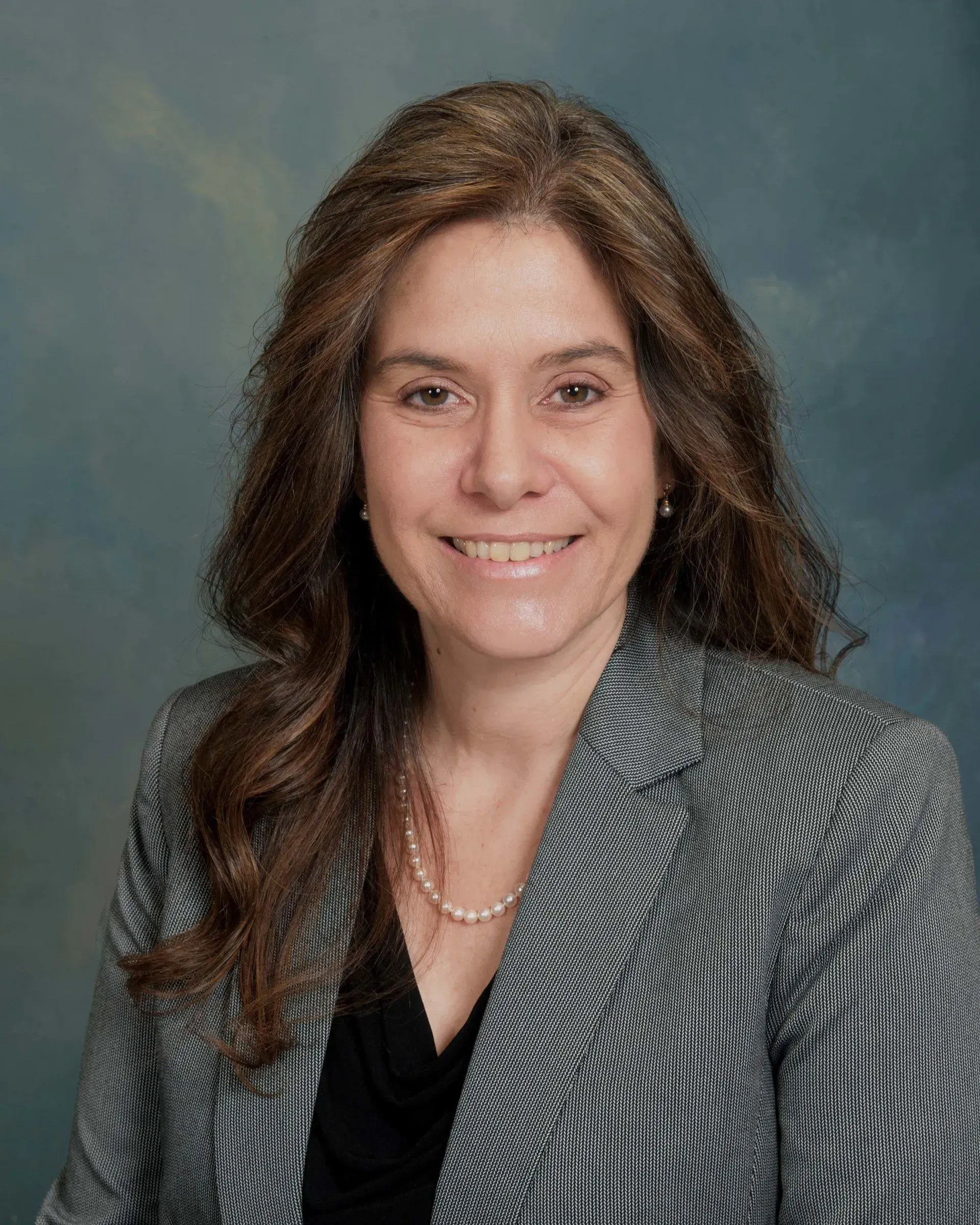 A woman wearing a jacket and a necklace is smiling for the camera.