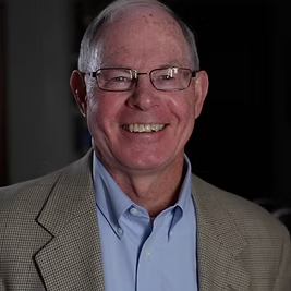 A man wearing glasses and a suit is smiling for the camera
