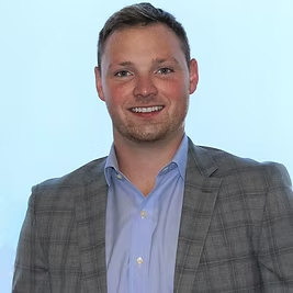 A man in a suit and blue shirt is smiling for the camera.