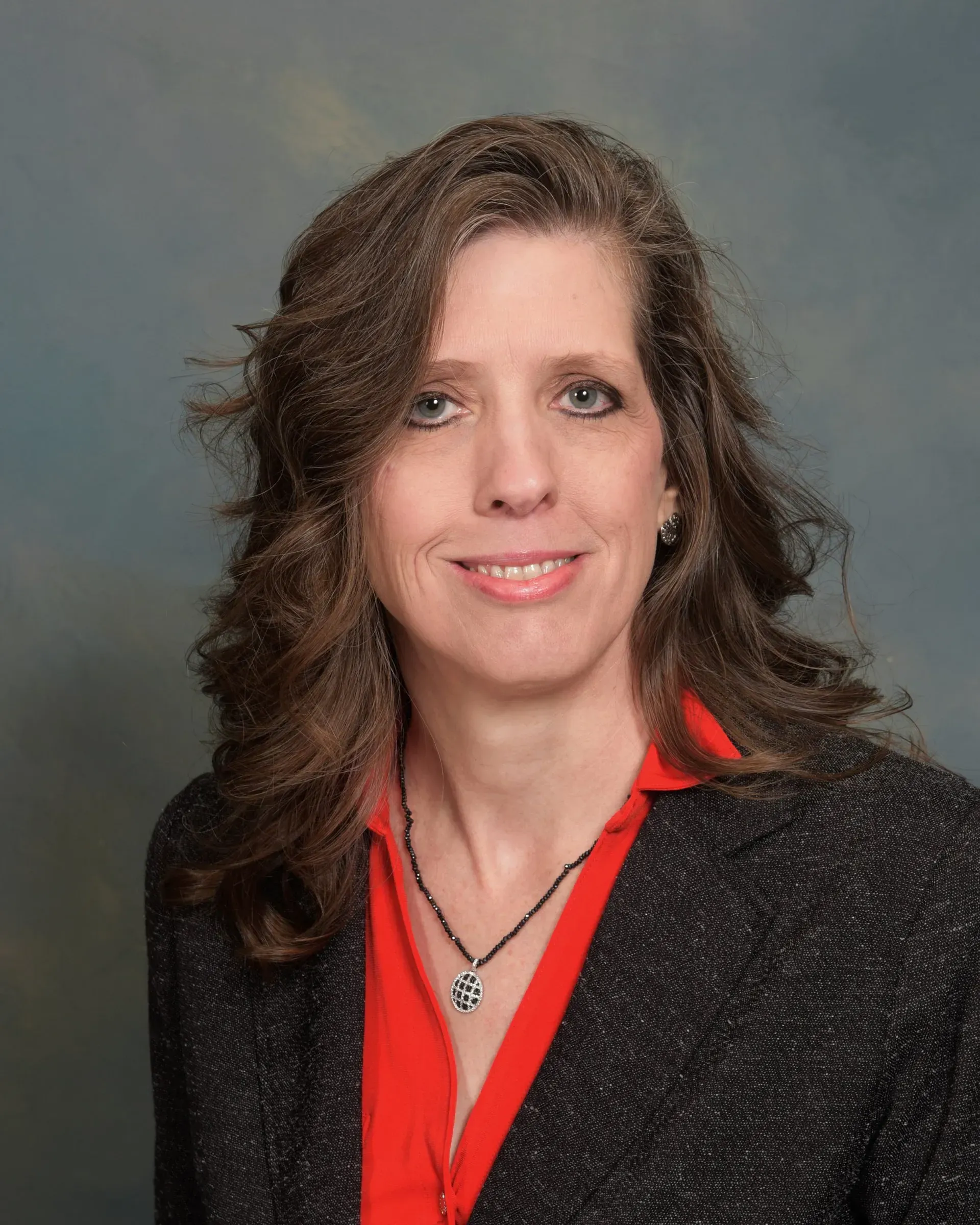 A woman wearing a black jacket and a red shirt is smiling for the camera.