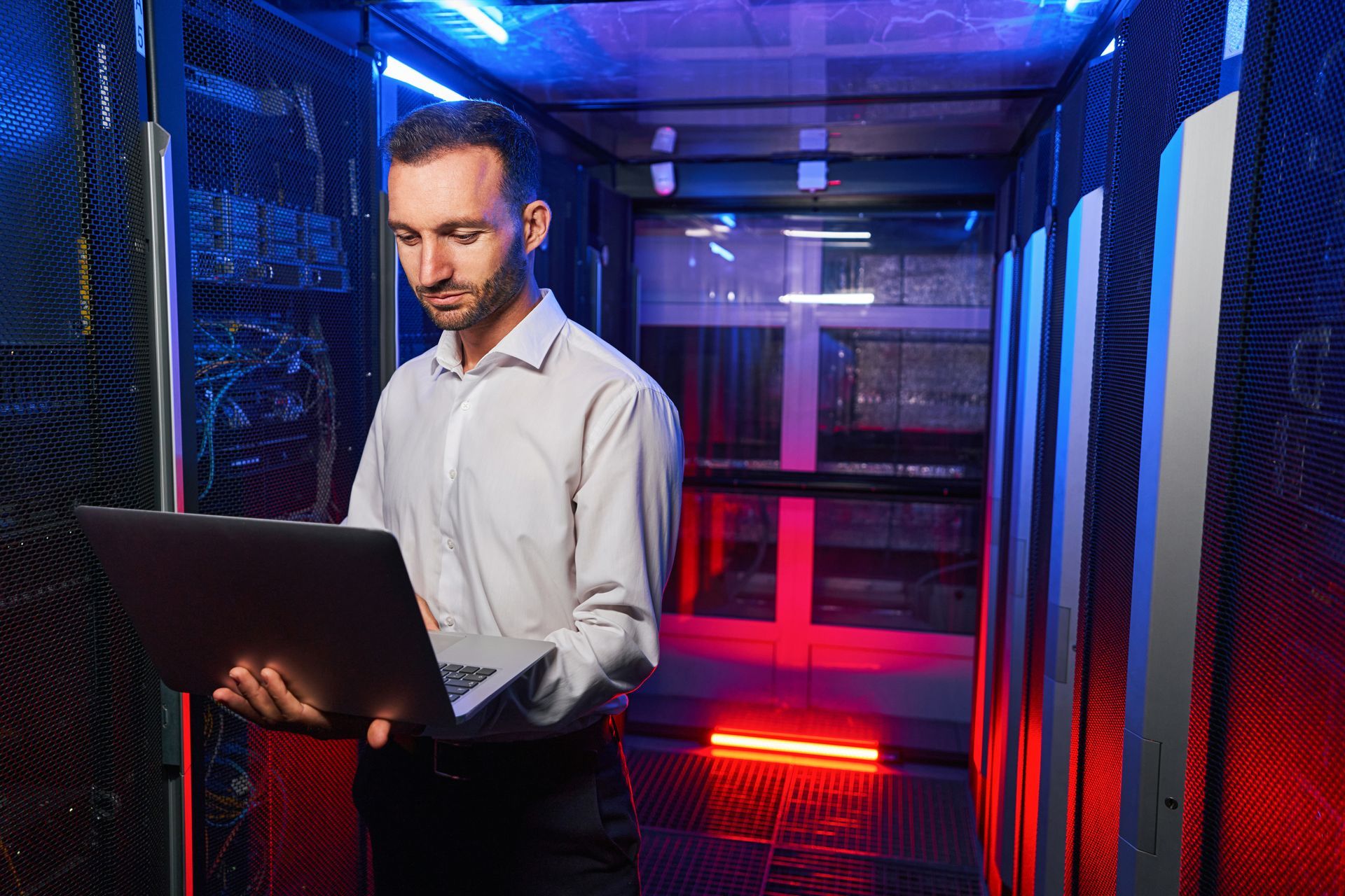 A man is using a laptop computer in a server room. 