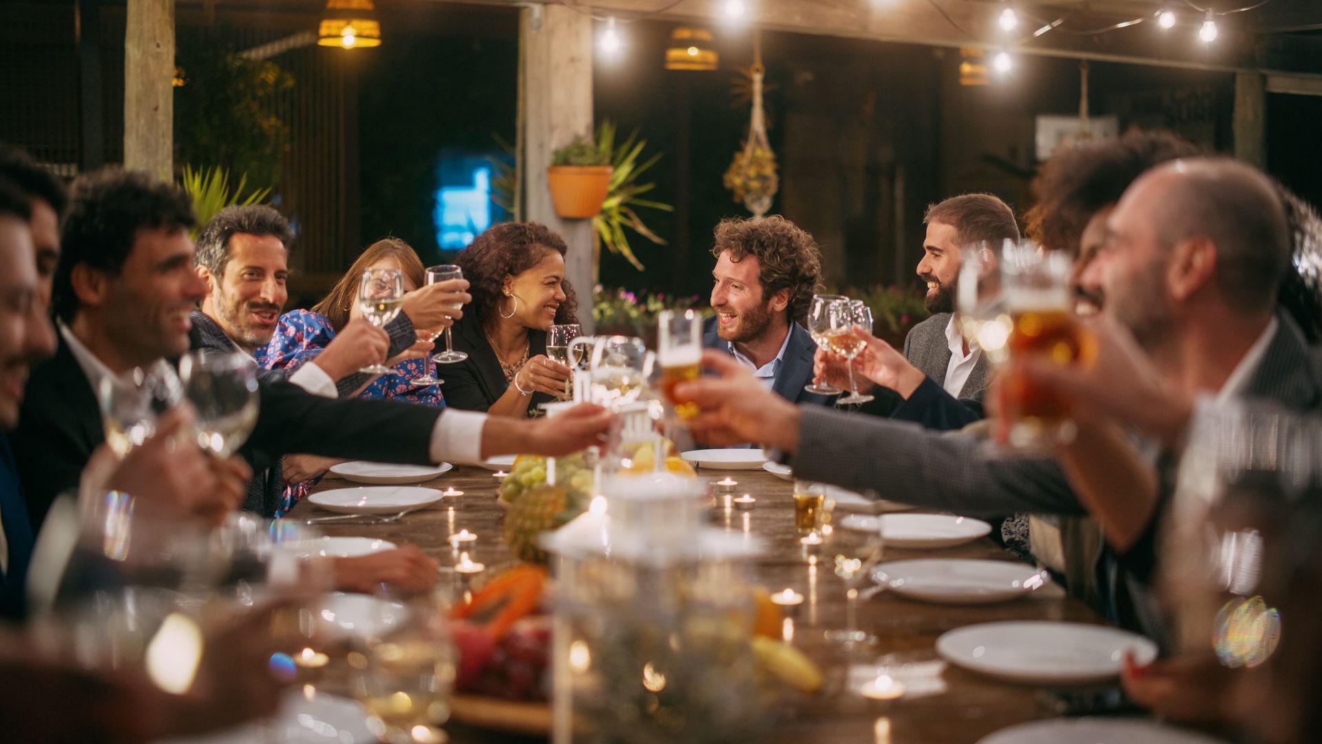 A group of people are sitting at a long table toasting with wine glasses. 