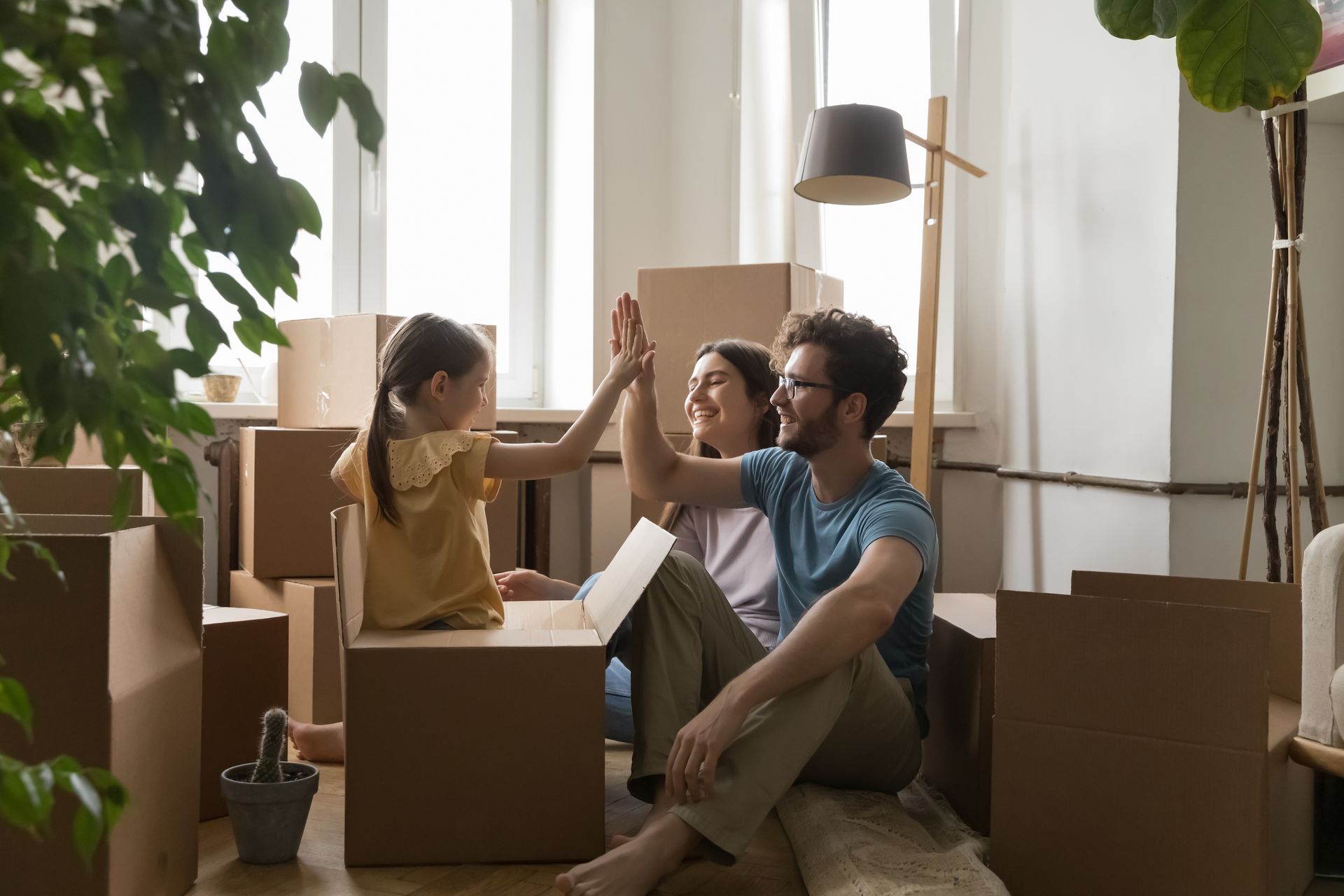 A family is giving each other a high five while sitting on the floor surrounded by cardboard boxes. 