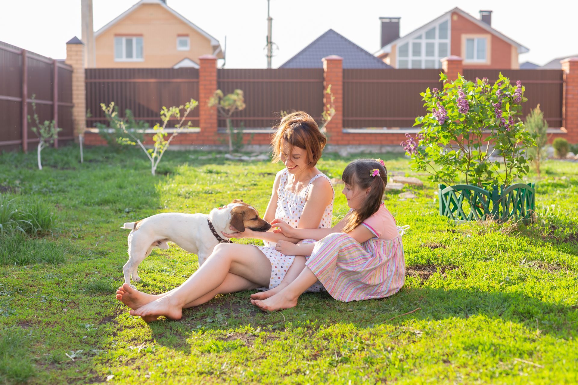 A woman and a little girl are sitting on the grass with a dog.